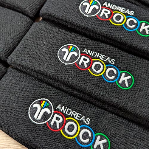 zu sehen sind schwarze Mützen bestickt mit dem Logo der Firma Andreas Rock, Kaminkehrer