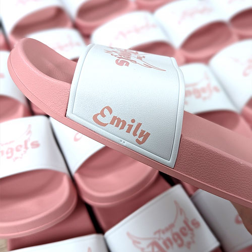 Zu sehen sind Badelatschen in rosa und weiß bedruckt mit einem Namen und dem Logo eines Vereins.