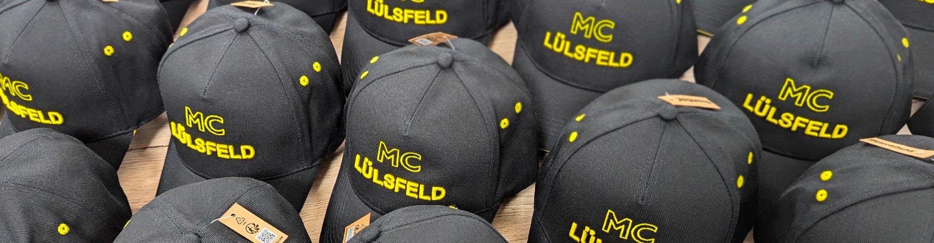 Zu sehen sind mehrere schwarze bestickte Caps mit eigenem Logo der Firma