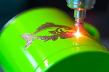 Das Bild zeigt eine grüne Tasse, auf die gerade mittels Lasergravur ein Motiv graviert wird