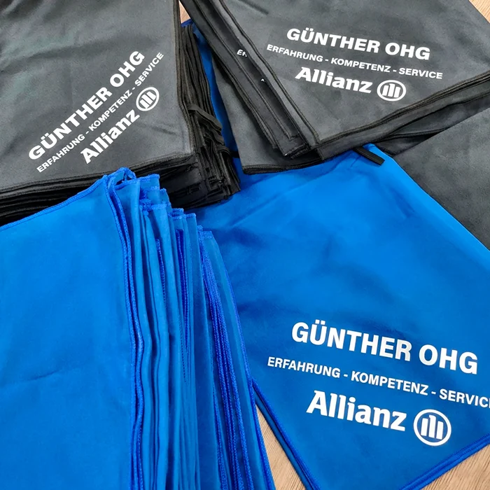 Stapel von blauen und grauen Handtüchern mit dem Branding von Allianz und Günther OHG.