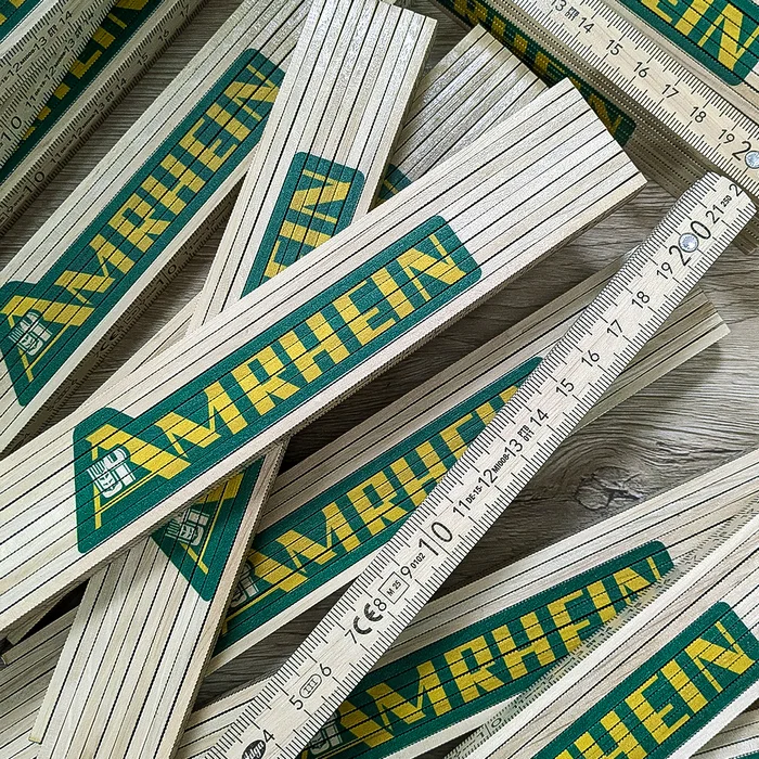 Personalisierte Textilien für Amrhein & Söhne – Projekt mit Lamasuli Schweinfurt 3 Eine Sammlung von Zollstöcken der Marke Amrhein, die auf einer hölzernen Oberfläche ausgebreitet sind.