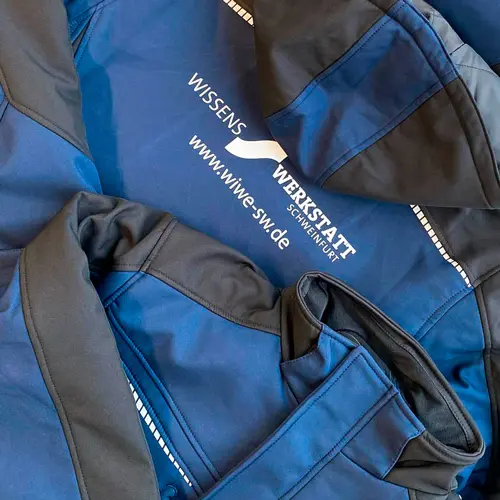 zu sehen ist Arbeitsjacke bedrucken lassen in blau/schwarz mit weißer Aufschrift