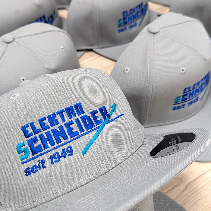 Graue Caps mit aufgesticktem Logo für Elektro Schneider Schweinfurt.