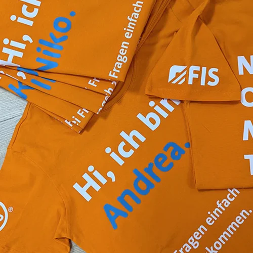 Mitarbeiterkleidung für FIS Informationssysteme und Consulting GmbH – Projekt mit Lamasuli Schweinfurt 2 Nahaufnahme von orangefarbenen T-Shirts mit DTF-Druck der Firma FIS, hergestellt von Lamasuli