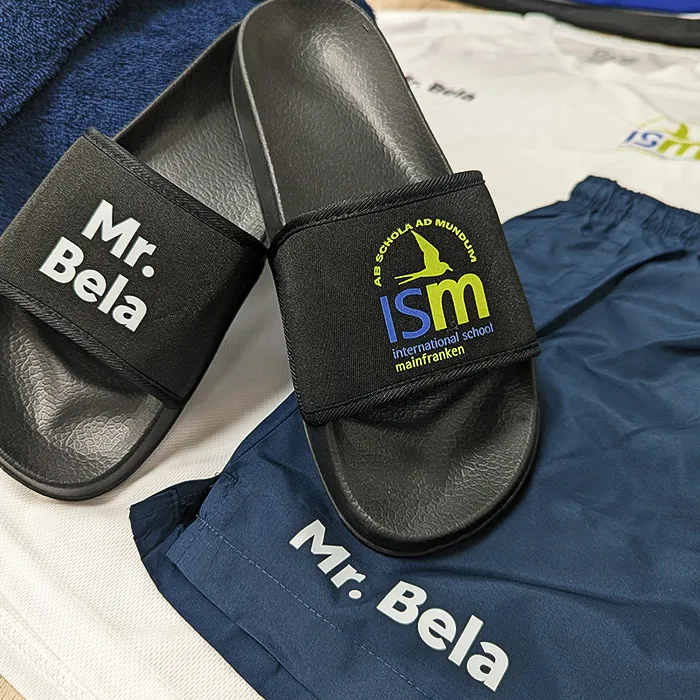 Schwarze Badelatschen mit ISM-Logo der International School Mainfranken in Schweinfurt