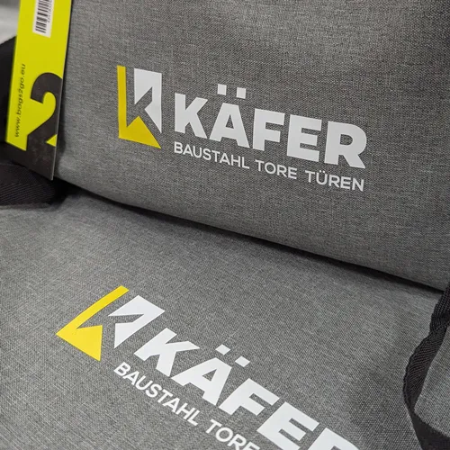 Reihe von grauen Laptoptaschen mit aufgedrucktem KÄFER Logo.
