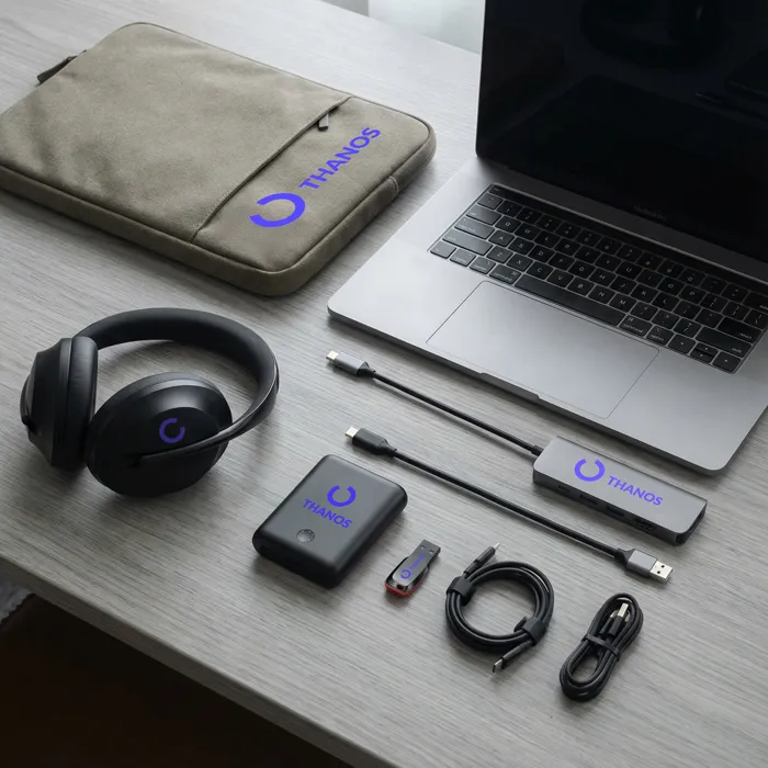 Set für mobiles Arbeiten: Laptop, Kopfhörer, Powerbank und diverse Adapter mit Thanos-Branding auf einem hellen Schreibtisch.
