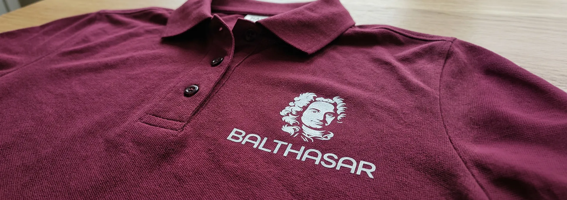 Startseite 66 Nahaufnahme eines bordeauxroten Poloshirts mit dem BALTHASAR-Logo auf der Brust, individuell bedruckt von Lamasuli.