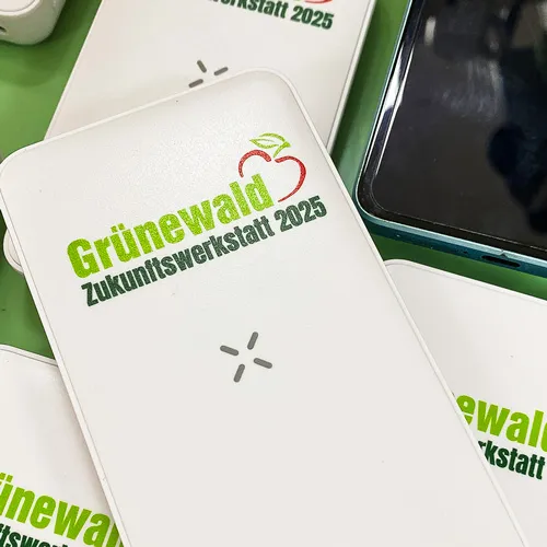 Detailaufnahme einer bedruckten Powerbank, die das grüne und rote Apfel-Logo der "Zukunftswerkstatt 2025" zeigt.