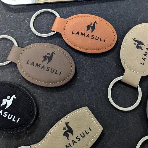 Nahaufnahme verschiedener Schlüsselanhänger aus Leder in Braun-, Schwarz- und Beigetönen mit graviertem "LAMASULI"-Logo und Lama-Symbol.