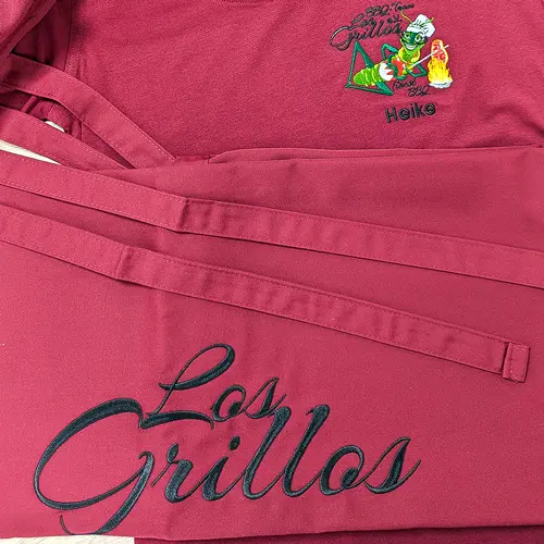 zu sehen ist eine bedruckte Grillschürze in rot, mit der schwarzen Aufschrift "Los Grillos"