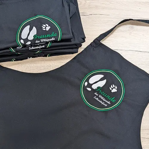 zu sehen ist eine bedruckte Schürze mit einem grün, weißen Logo