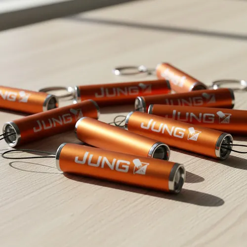 Mehrere orangefarbene Schlüsselanhänger-Taschenlampen mit dem weißen "JUNG"-Logo liegen auf einer hellen Holzoberfläche.