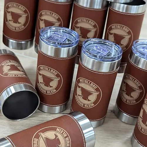 Stapel von personalisierten Edelstahl-Thermobechern mit braunem Leder-Finish, versehen mit einem Amboss-Logo und der Aufschrift „Metallbau Joshua Klein“.