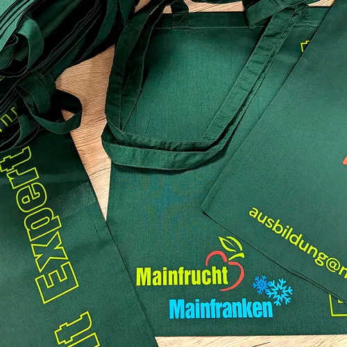 zu sehen sind dunkelgrüne bedruckte Taschen, mit gelber und hellblauer Schrift "Mainfrucht Mainfranken"